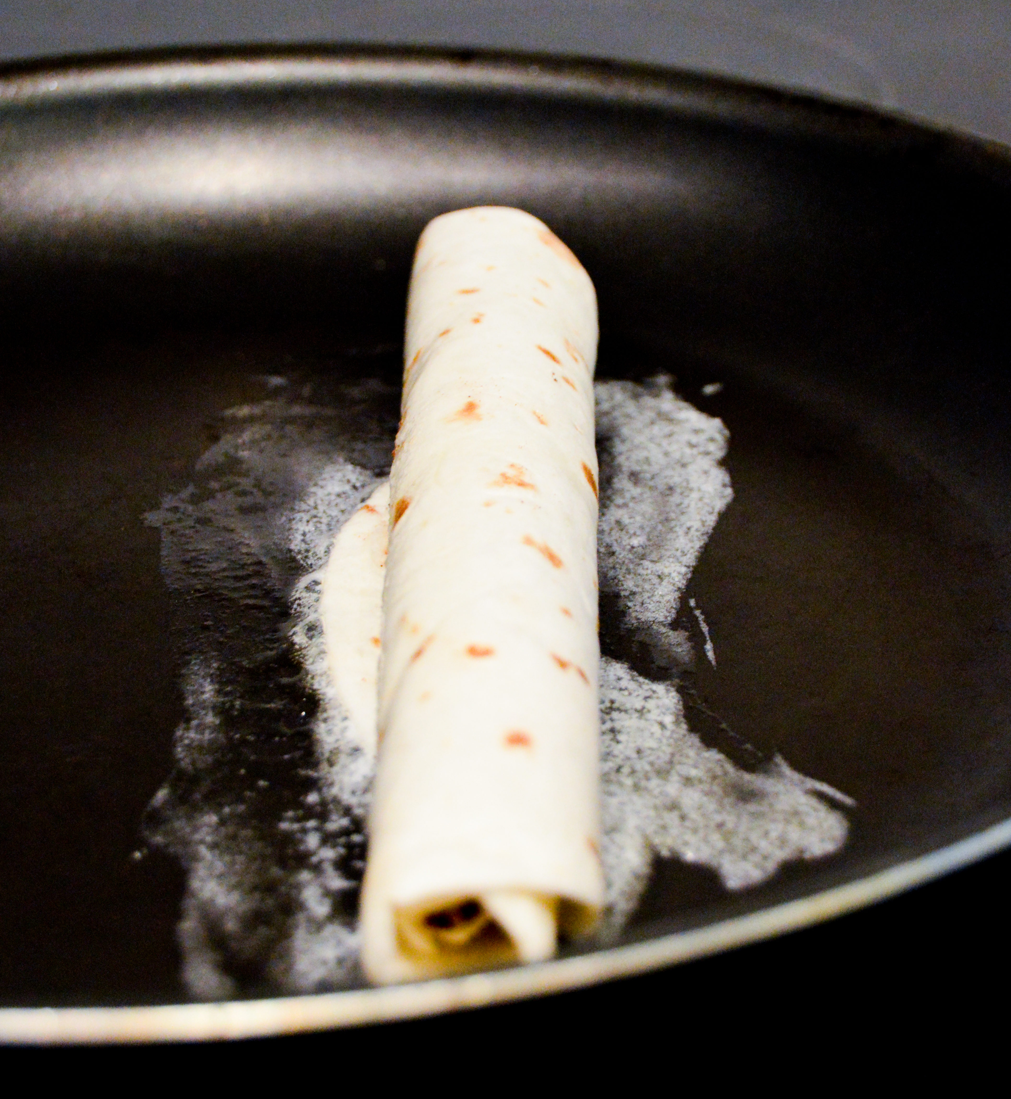 Brown tortilla roll up in melted butter in frying pan.