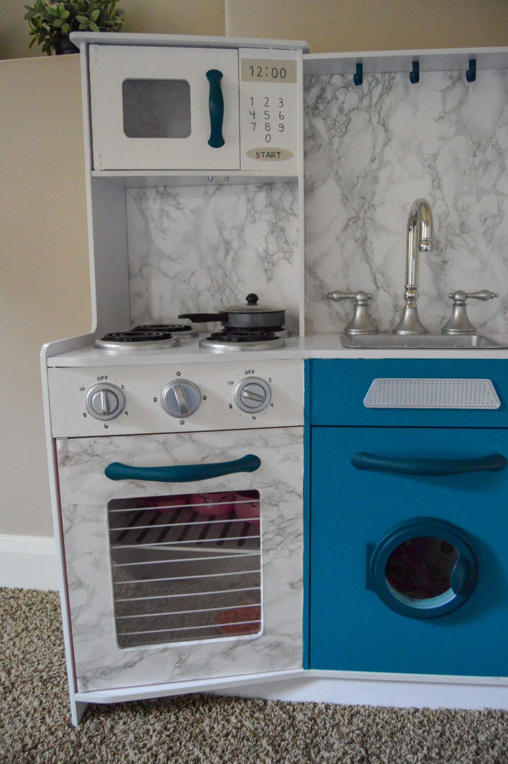 How to do a play kitchen makeover. Paint, wallpaper, and revive an old play kitchen to make it look cute and modern. Marble and wood wallpaper, teal paint, and white paint. Plus our kids' playroom nursery reveal.