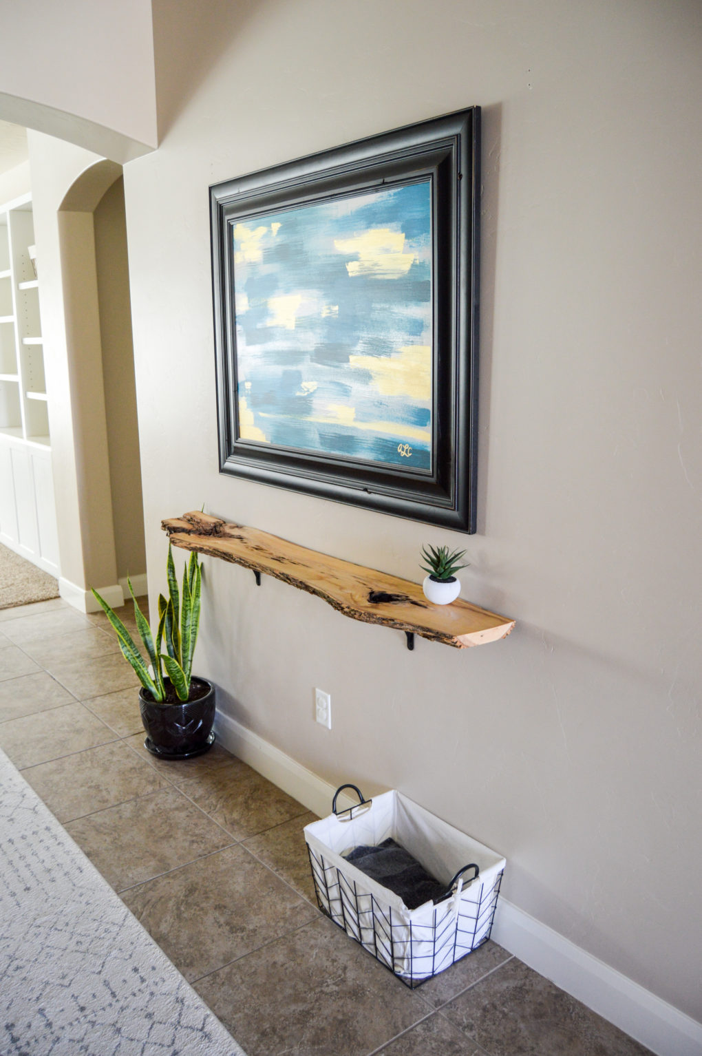 Live edge wood shelf in long hallway entry. Large modern art. Industrial modern look with a boho vibe.
